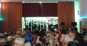 Blick in die Mehrzweckhalle. Auf der Bühne der Kirchenchor.